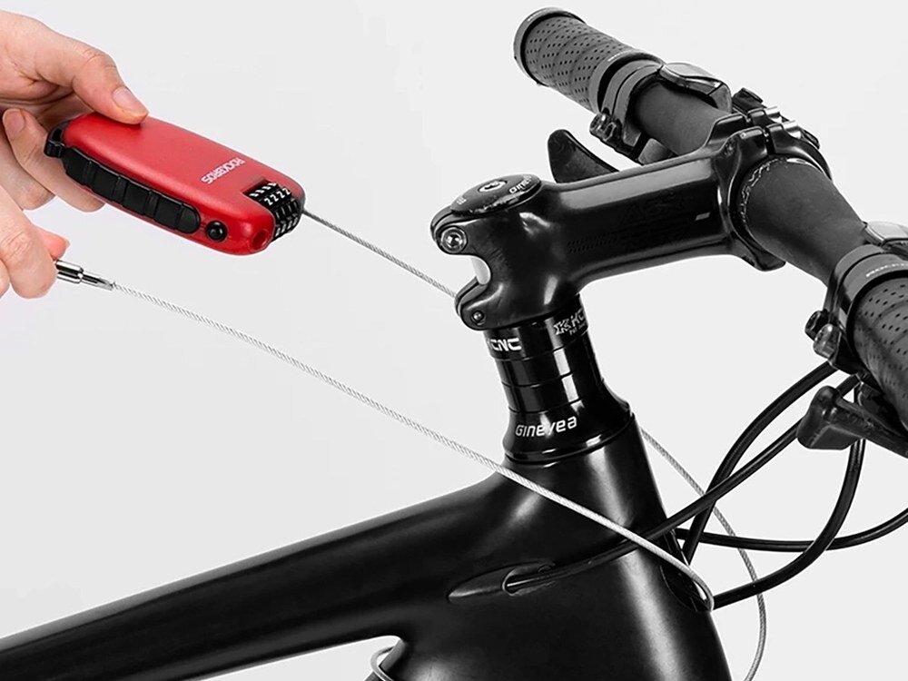 Osoba trzyma czerwone zapięcie rowerowe z widocznym logo \'ROCKBROS\', które jest przymocowane do kierownicy roweru za pomocą stalowej linki.