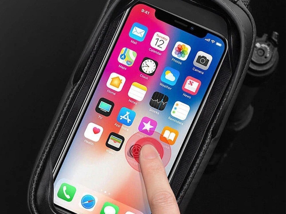 Smartfon z kolorowym ekranem dotykowym umieszczony w przezroczystej kieszeni torby rowerowej. Na ekranie widoczne są ikony aplikacji, a palec dotyka jednej z nich.