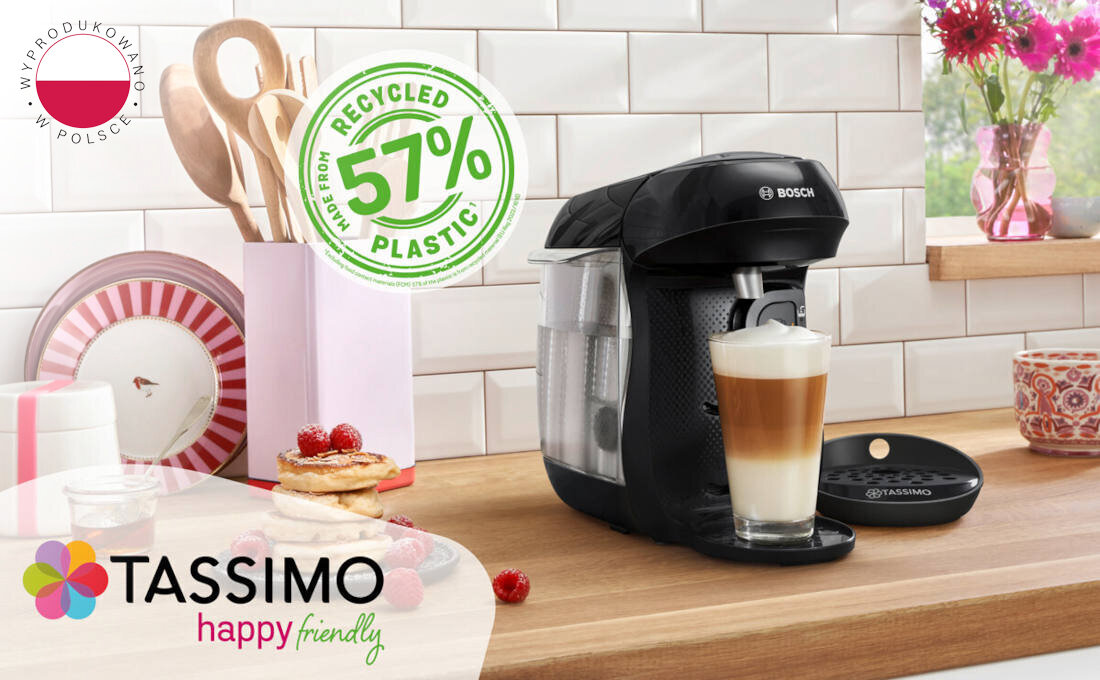 Czarny ekspres do kawy BOSCH Tassimo stoi na blacie kuchennym, obok filiżanki z kawą. Na obrazie widoczne są napisy: \'Wyprodukowano w Polsce\', \'Made from 57% recycled plastic\', oraz logo \'TASSIMO happy friendly\'.