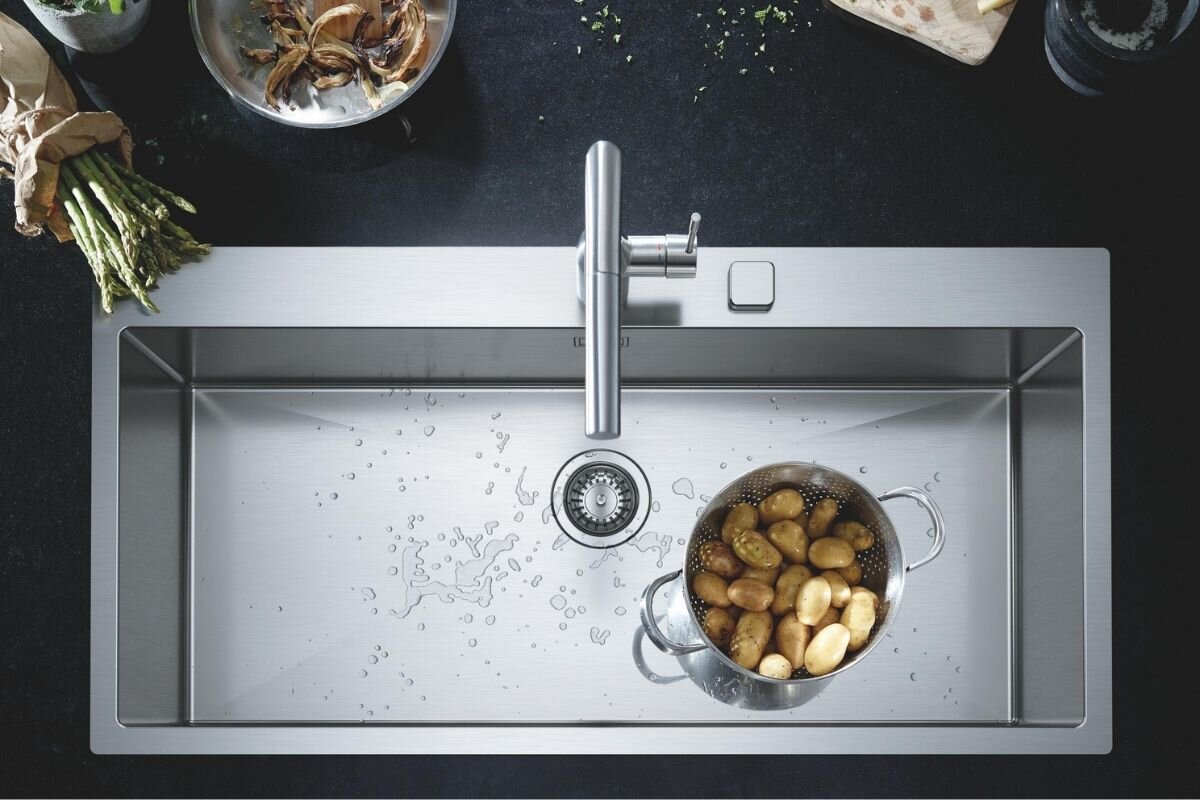 BATERIA KUCHENNA GROHE ESSENCE 30270DC0 STAL SZCZOTKOWANA Widok z góry na stalowy zlew z długą komorą i baterią, w którym znajduje się cedzak z ziemniakami trwałość powłoka PVD odporność precyzja czyszczenie