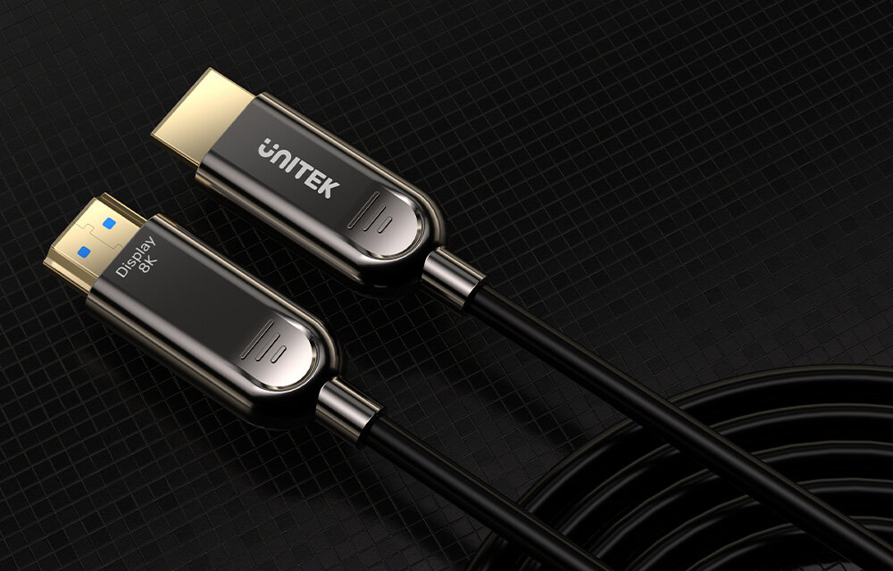 Na obrazie widoczne są dwa końce kabla HDMI z metalowymi złączami, na jednym z nich znajduje się napis \'UNITEK\', a na drugim \'Display 8K\'. Kabel jest czarny i zwinięty na ciemnym tle.