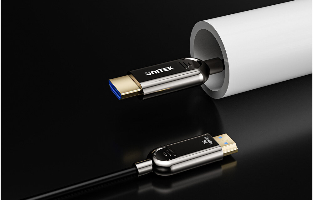 Na obrazie widoczny jest kabel HDMI z metalowymi końcówkami, z logo \'UNITEK\' na jednej z nich. Kabel jest częściowo włożony w biały, cylindryczny obiekt.