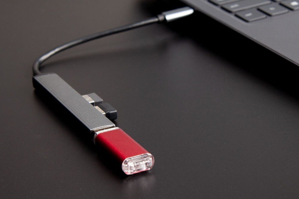 Hub ORICO AH-13-GY-EP-HW Adapter USB-C z podłączonym czerwonym pendrive'em i dwoma innymi akcesoriami USB, podłączony do laptopa na czarnym biurku, kompatybilność, systemy, przewód, długość