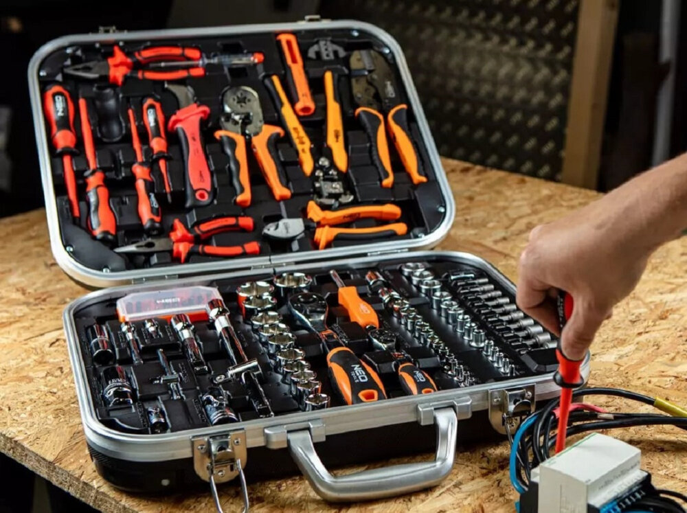 Zestaw narzędzi NEO TOOLS 01-310 otwarta walizka z zestawem na drewnianym blacie obok dłoń osoby elektryczne 108 elementów walizka certyfikat 1000V