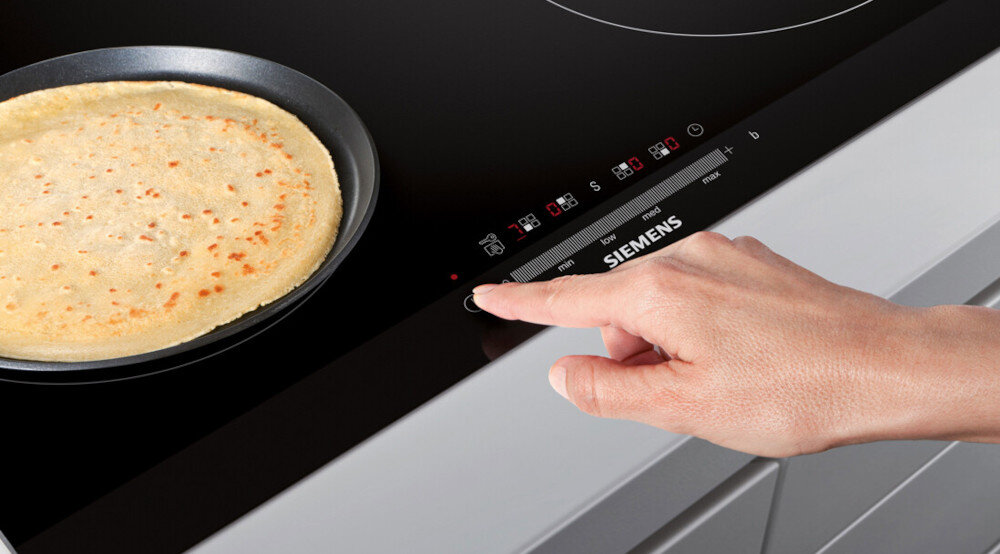 PŁYTA SIEMENS EE611BPB5E Na zdjęciu widać płytę indukcyjną Siemens, na której na patelni smaży się naleśnik. Dłoń osoby obsługującej płytę dotyka suwaka mocy na podświetlonym panelu sterowania, regulując temperaturę smażenia reStart reStart przywracanie ustawień szybkie wygodne komfort spokój intuicyjne bezproblemowe gotowanie