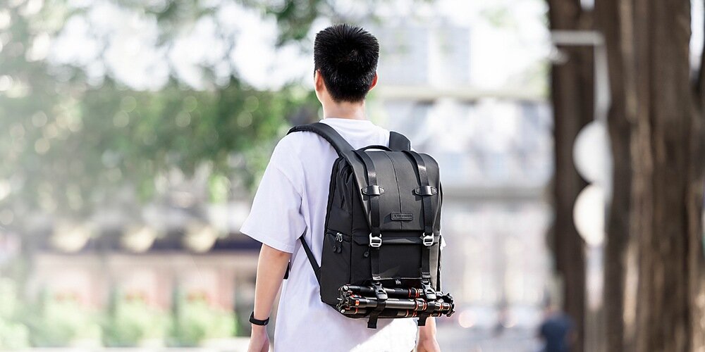 Mężczyzna od tyłu z plecakiem K&F idzie, w tle rozmyte góry i jasne niebo