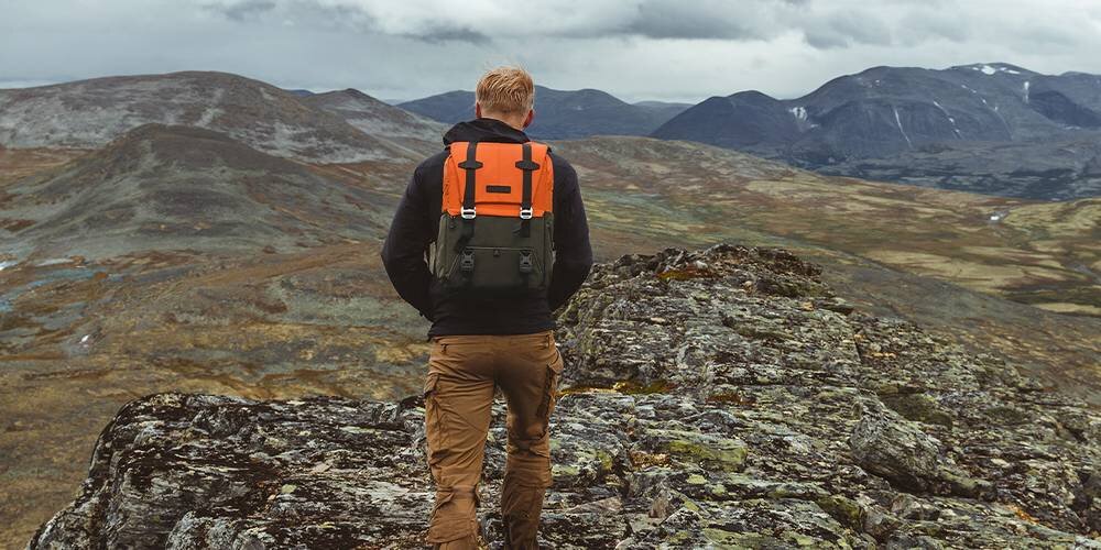 Mężczyzna od tyłu z plecakiem K&F idzie, w tle rozmyte góry i jasne niebo