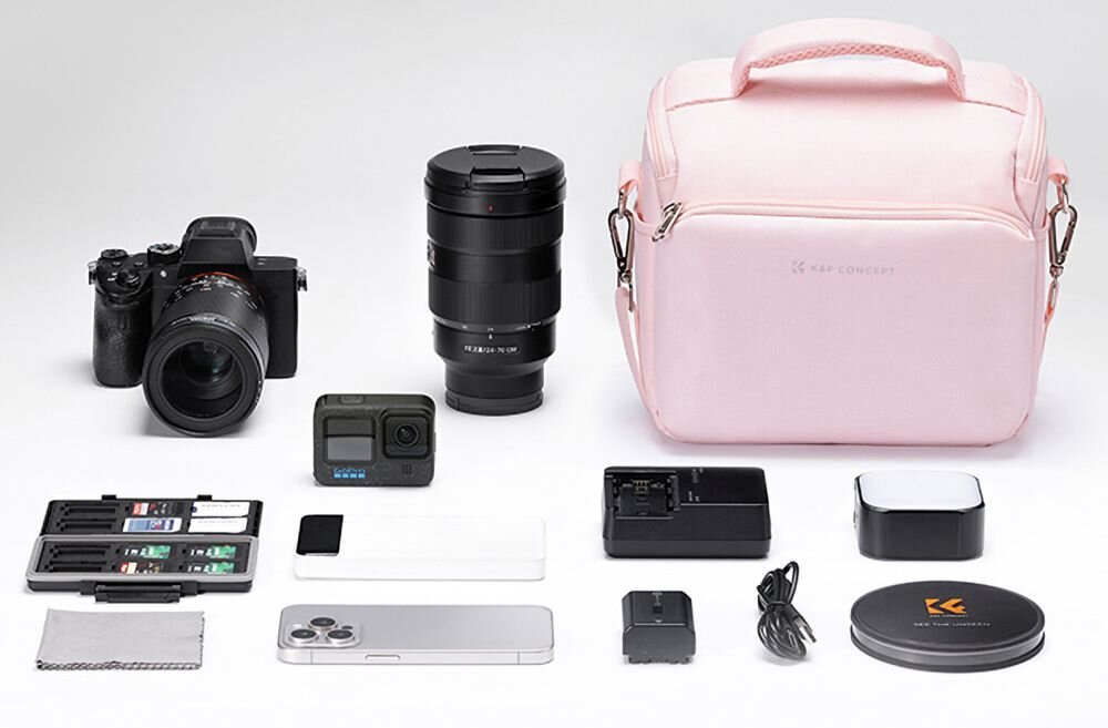 Na obrazie widoczna jest różowa torba z napisem \'K&F CONCEPT\', obok której znajdują się aparat fotograficzny, obiektyw, kamera sportowa, ładowarka, smartfon, kable oraz inne akcesoria fotograficzne. Wszystkie przedmioty są ułożone na białym tle.