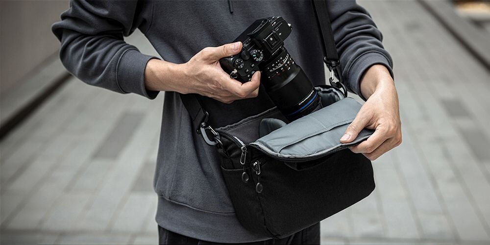 Mężczyzna chowa aparat z obiektywem do przewieszonej przez ramię torby K&F Concept Camera Sling Bag