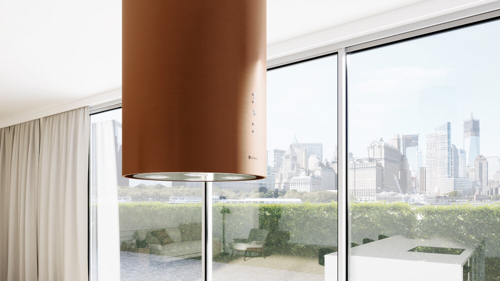 OKAP GLOBALO CYLINDRO ISOLA 39.7 MIEDŹ MAT Zdjęcie przedstawia kuchnię z wyspą wyposażoną w płytę grzewczą. Nad wyspą zamontowany jest okap w kształcie miedzianej tuby z czterema wbudowanymi lampkami LED. W centralnym miejscu na wyspie stoi roślina w doniczce, a w tle widać eleganckie, połyskujące szafki oraz detale kuchenne. Całość utrzymana jest w jasnej, minimalistycznej aranżacji z kontrastowym miedzianym akcentem wyspowy globalo miedziany stal szlachetna tuba kuchenny sufitowy design premium wyspa cylindryczny elegancki kuchnia agd wydajny dekoracyjny