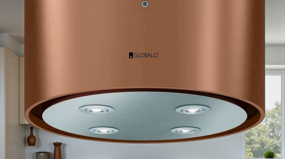 OKAP GLOBALO CYLINDRO ISOLA 39.7 MIEDŹ MAT Zdjęcie przedstawia okap kuchenny w kształcie miedzianej tuby firmy Globalo, widziany od dołu. Na spodzie urządzenia znajdują się cztery wbudowane lampki LED rozmieszczone symetrycznie. W tle widoczne są elementy kuchni: zlew, rośliny w doniczkach, drewniane deski oraz piekarnik. Kompozycja podkreśla elegancki wygląd, solidne wykonanie i funkcjonalne oświetlenie okapu światło power led 4200k regulacja barwy światła 2900k 6300k oświetlenie kuchenne dopasowanie nastroju okap oświetlenie robocze oświetlenie