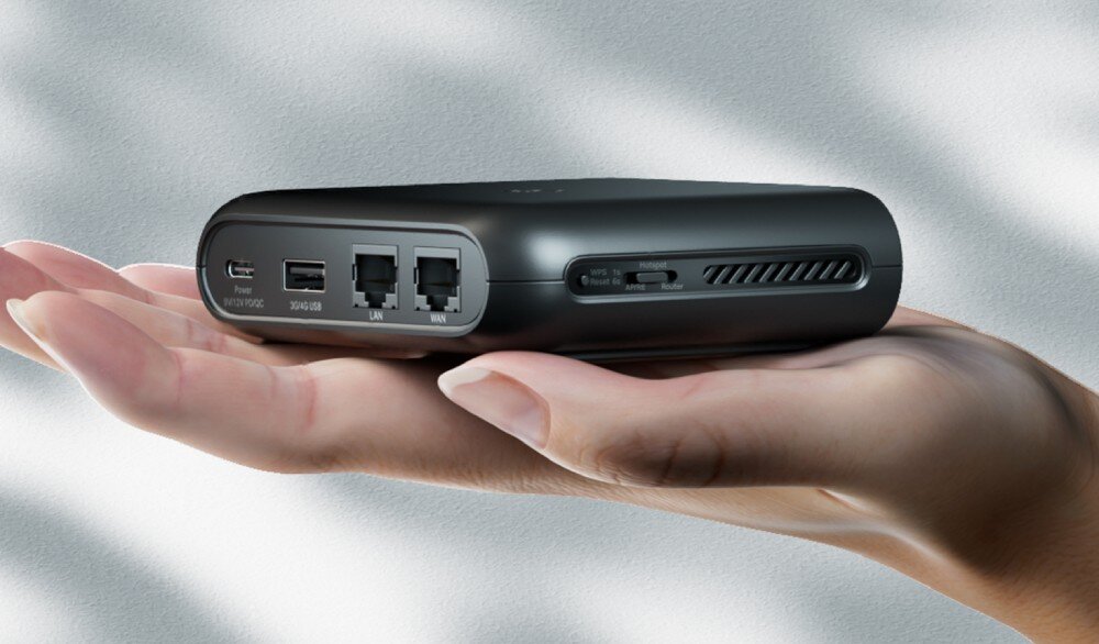 Router TP-LINK TL-WR1502X Dłoń trzyma czarny, kompaktowy router z widocznymi portami: USB-C, USB 2.0, LAN i WAN. Na boku urządzenia znajduje się suwak do zmiany trybów pracy, złącza ethernet