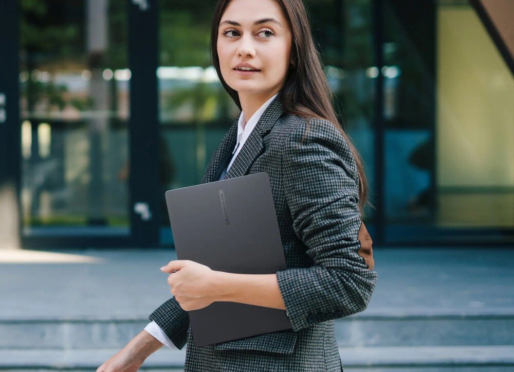 Laptop ASUS ExpertBook B1403CVA-S60475X Kobieta w eleganckim stroju biznesowym trzyma zamknięty laptop w jednej ręce, idąc po schodach na tle budynku z przeszkleniami, bateria, ładowanie, zasilacz