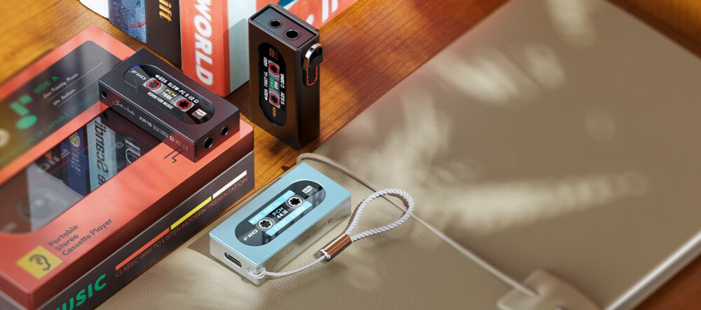 Wzmacniacz słuchawkowy FIIO KA15 kolory midnight black niebieski otwór na smycz stylowy design, wzmacniacz leżący na aktówce oraz drugi w innej wersji kolorystycznej leżący na pudełkach od płyt CD
