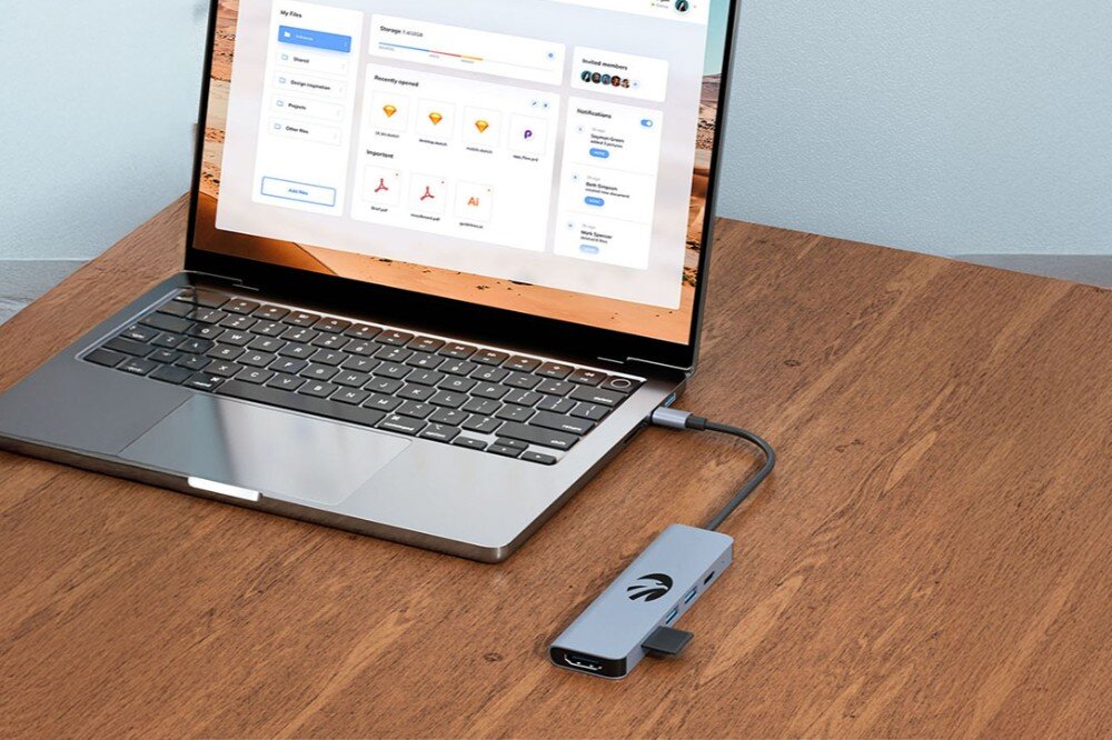 Hub HAWK HW-HUB601 6w1 Laptop na drewnianym biurku z otwartym oknem menedżera plików na ekranie. Do laptopa podłączony jest hub USB-C, a w jego gnieździe widoczna jest karta pamięci, czytnik kart pamięci