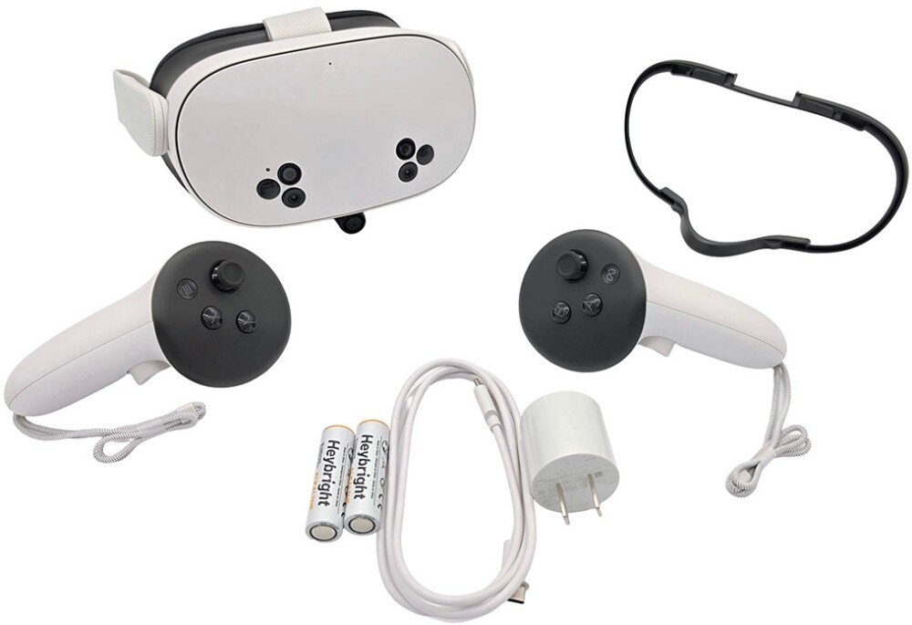 Na obrazie widoczne są gogle VR z białą obudową, dwa kontrolery, dwie baterie, kabel zasilający oraz adapter. Obok gogli znajduje się czarny element, prawdopodobnie część mocująca.
