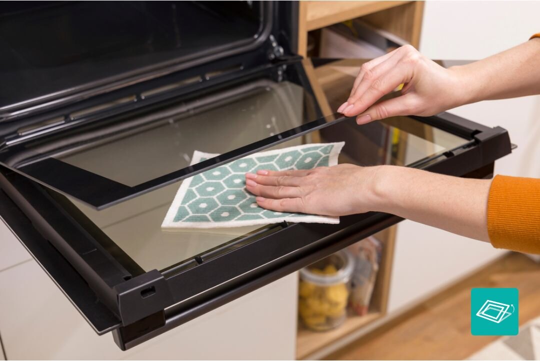 PIEKARNIK GORENJE BO6635E01B Czyszczenie wewnętrznej strony drzwi piekarnika przy użyciu ściereczki, przy całkowicie otwartym froncie. Ujęcie podkreśla łatwy dostęp i prostą pielęgnację gładkiej szklanej powierzchni