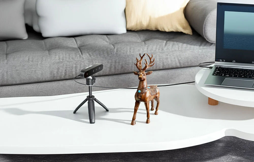 Skaner 3D CREALITY CR-Scan Ferret SE  prezentacja urządzenia obok figurka jelenia na stoliku w tle widoczny kawałek laptopa i kanapa opracowany z myślą o osobach rozpoczynających pracę z modelowaniem digitalizacja obiektów skanowanie w kolorze