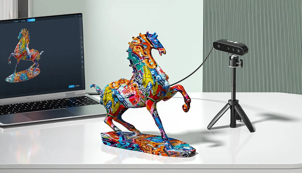 Skaner 3D CREALITY CR-Scan Ferret SE  prezentacja urządzenia obok figurka konia na stoliku w tle widoczny kawałek laptopa kamera 24-bit rejestrowanie kształtu i wyglądu w kolorze