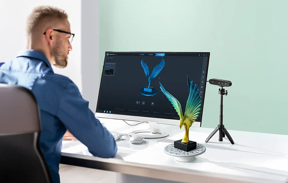 Skaner 3D CREALITY CR-Scan Ferret SE  prezentacja urządzenia obok figurka i monitor z włączonym programem przy biurku siedzący mężczyzna ekosystem Creality spójny łańcuch szybkie testowanie