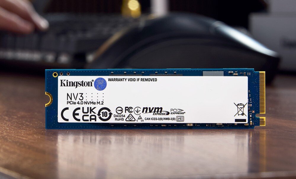 Na obrazie widoczny jest dysk SSD z oznaczeniem Kingston NV3 PCIe 4.0 NVMe M.2. Na etykiecie znajdują się różne certyfikaty i ostrzeżenia, w tym CE, UKCA, RoHS oraz informacja \'WARRANTY VOID IF REMOVED\'.