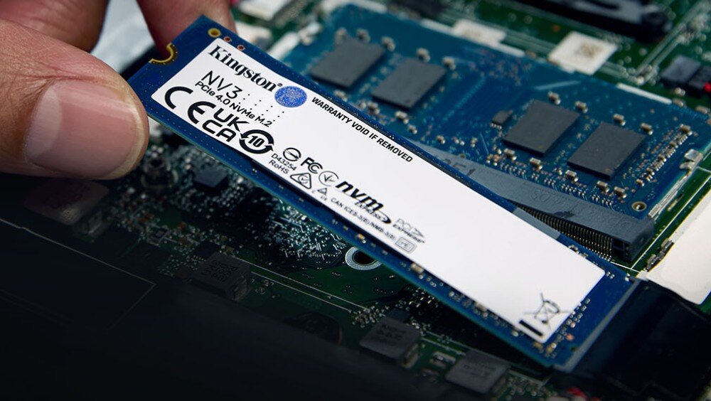 Osoba trzyma dysk SSD Kingston NV3 500GB z widocznymi oznaczeniami CE i NVMe. W tle widać elementy płyty głównej komputera.