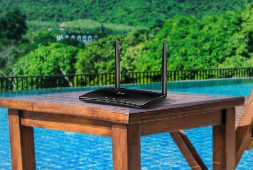Router TP-LINK Archer MR202 4G LTE Czarny router z dwiema antenami stojący na drewnianym stole na tle basenu i zielonych drzew, opis