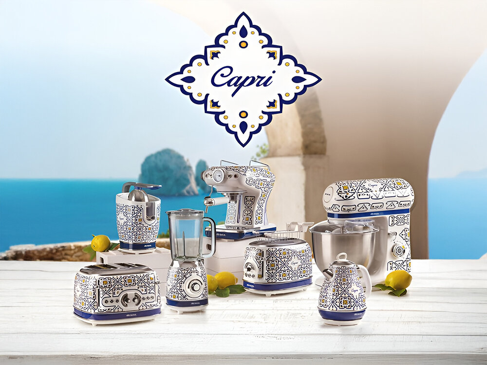 Wyciskarka do cytrusów ARIETE Capri 413 jasne tło wyspy na blacie sprzęty w biało niebieskiej kolorystyce wyciskarka tostery blender robot planetarny ekspres czajnik Linia Capri włoska elegancja i praktyczność Morze Śródziemnomorskie radosna atmosfera południowych Włoch krystalicznie błękitne fale słoneczny urok regionu odrobina śródziemnomorskiego uroku unikalna kolekcja wyrafinowany styl funkcjonalność