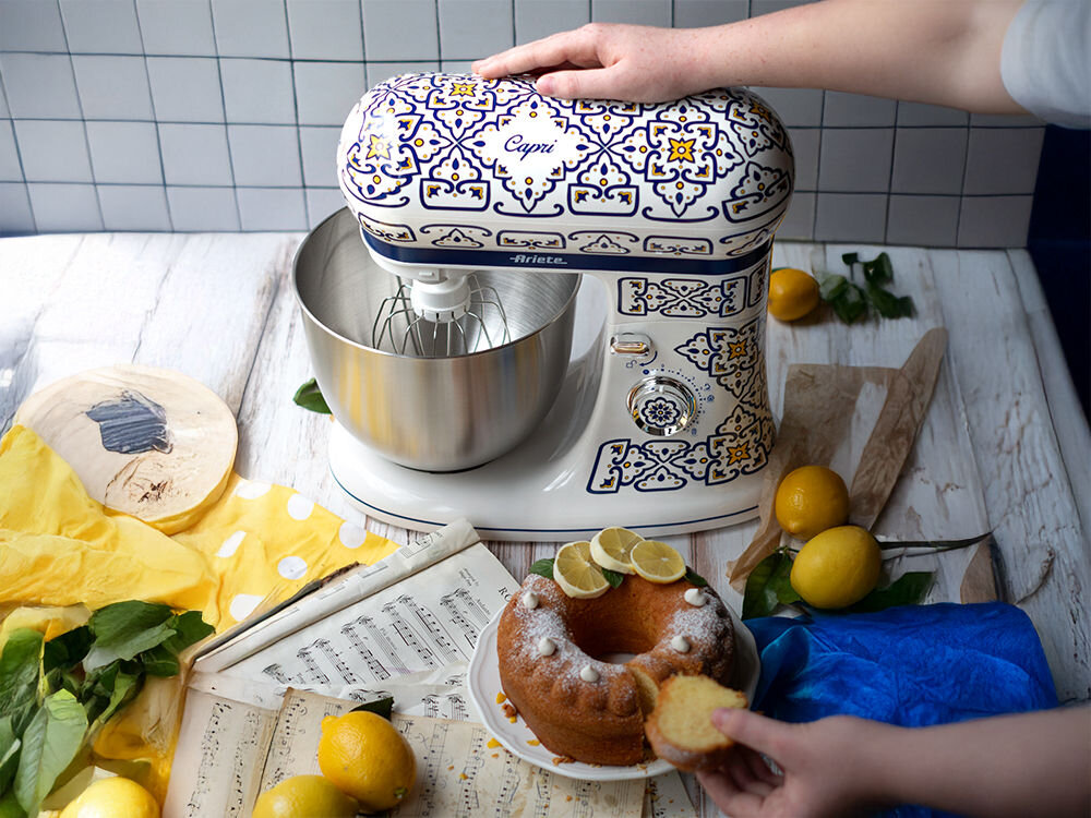 Robot kuchenny planetarny ARIETE 1588 Capri 2400W kolorowy robot wzorzysta obudowa biało niebieska z elementami żółtego pokrętło mieszadło osoba trzyma rękę na obudowie obok stoi babka 42,5 cm x 28,5 cm x 38,5 cm wydajność śródziemnomorski styl Silnik o mocy 2400 W regulacja prędkości od 30 do 172 obrotów na minutę misa o pojemności 5,5 litra radzi sobie z każdym wyzwaniem do mieszania, ubijania i zagniatania biało-niebieska kolorystyka z żółtymi akcentami