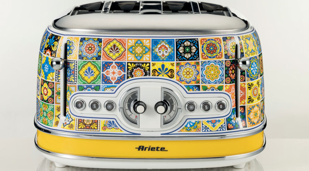 Toster Ariete 1560P wzorzysty toster otwory nóżki przyciski jasne tło śródziemnomorskie krajobrazy elegancka konstrukcja słoneczne barwy mozaika lazurowe wybrzeża słońce Italii kompaktowy rozmiar 30 x 19 x 20 cm chrupiące tosty gorące kanapki szybkie rozmrażanie estetyka praktyczność towarzysz codziennych kulinarnych przyjemności moc 810 W