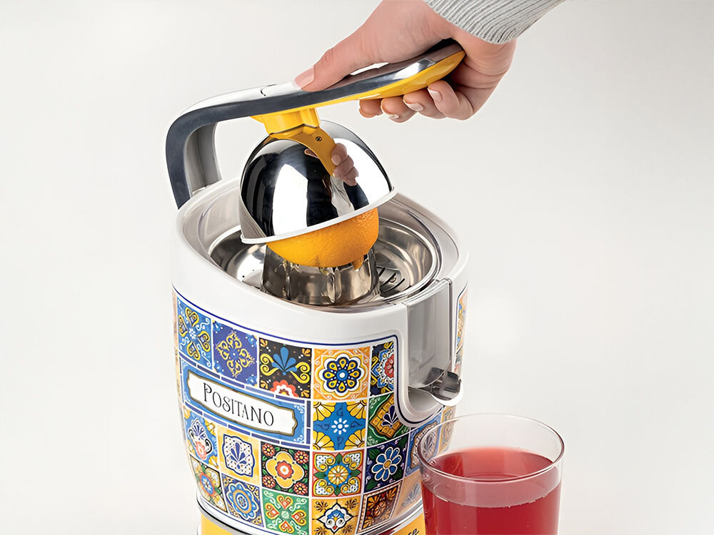 Wyciskarka do cytrusów ARIETE Positano 413 jasne tło wyciskarka biało niebieska kolorystyka obudowy mozaika metalowe elementy osoba wyciska sok z grejpfruta czerwony sok w szklance Ergonomiczna dźwignia maksymalny komfort użytkowania efektywne wyciskanie soku dwa stożki o różnych rozmiarach mniejszy do cytryn i limonek większy pomarańcze grejpfruty wszechstronna świeże i aromatyczne soki