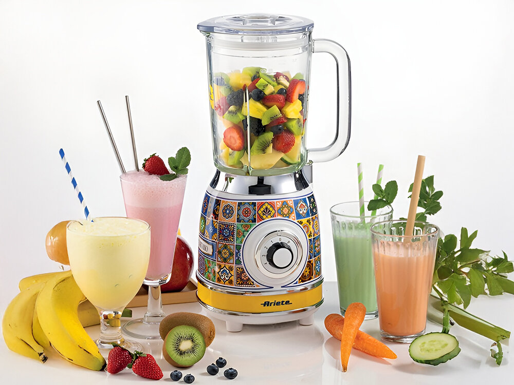 Blender kielichowy ARIETE 583 Positano białe tło blender przeźroczysty kielich pokrętło wzorzysta obudowa biało niebieska z elementami żółtego owoce wewnątrz blendera kolorowe koktajle w szklankach owoce i warzywa zdrowe potrawy i napoje odżywcze smoothie koktajle mleczne kremowe zupy pokrojenie składników umieszczenie ich w pojemniku wybranie odpowiednich ustawień prędkości pełne witamin dania