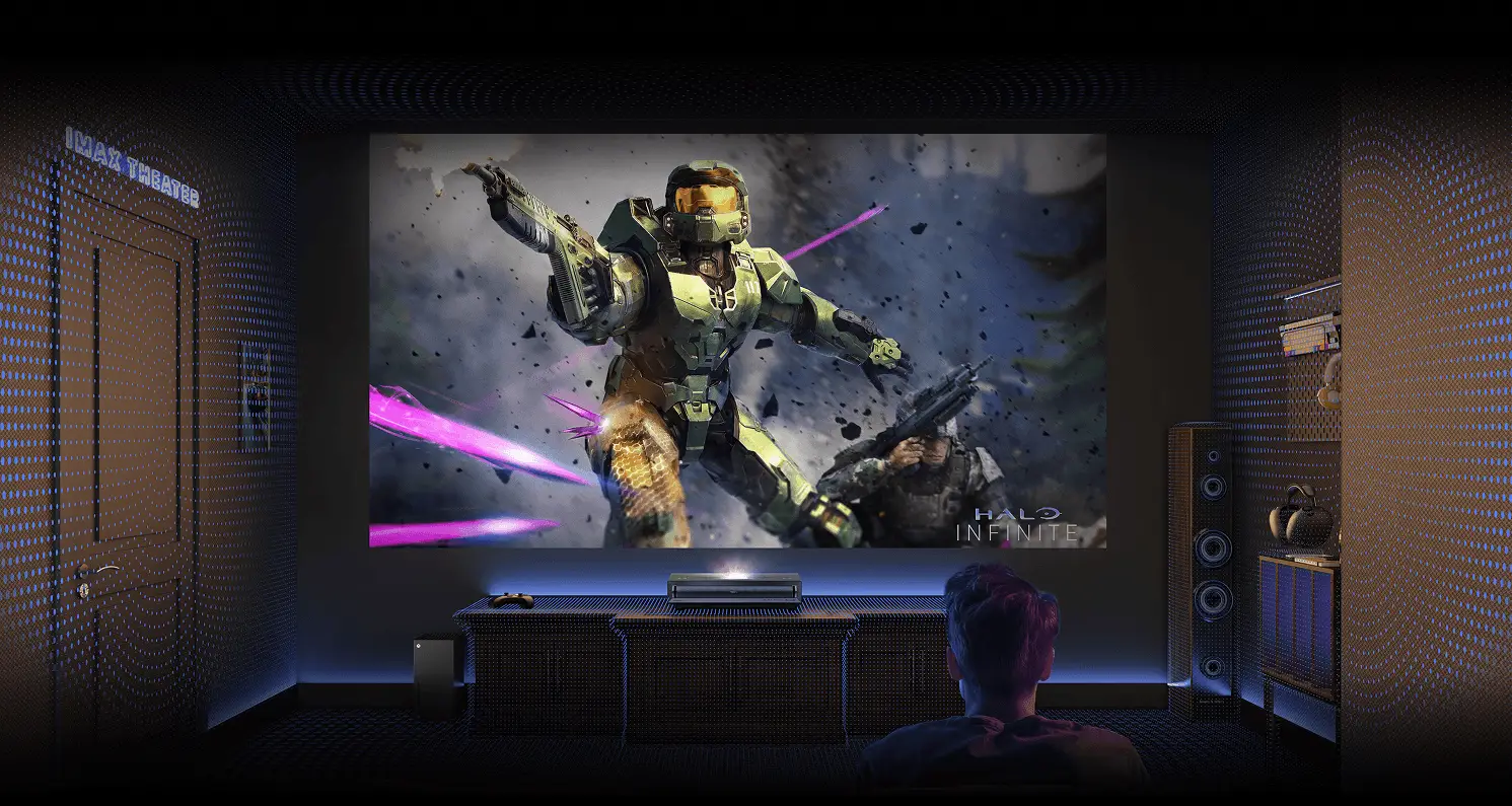 Widok zza gracza na ekran z Master Chiefem z gry Halo Infinite. Cały pokój pokryty siatką niebieskich punktów świetlnych.