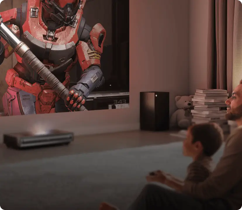 Mężczyzna i dziecko na dywanie grają w Halo Infinite. Projektor Hisense wyświetla na ścianie postacie w pancerzach.