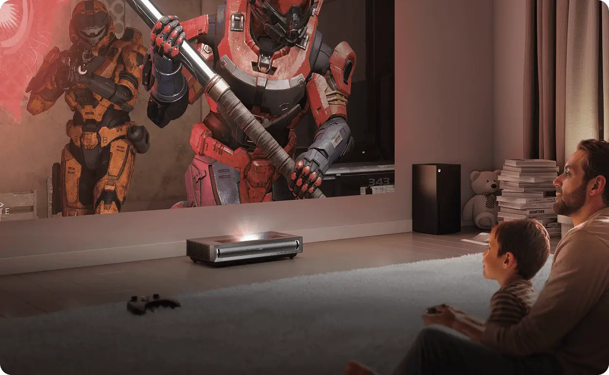 Mężczyzna i dziecko na dywanie grają w Halo Infinite. Projektor Hisense wyświetla na ścianie postacie w pancerzach.