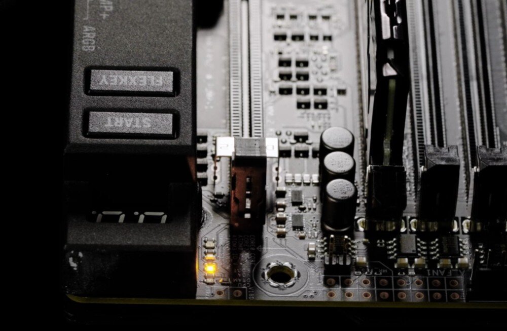 Płyta główna ASUS ROG Maximus Z890 Extreme Fragment płyty głównej z przyciskami „Start” i „FlexKey” na bocznej krawędzi oraz slotami pamięci RAM. Obok złącza zasilania znajduje się podświetlony na żółto wskaźnik diagnostyczny, ułatwiony montaż, rozwiązania