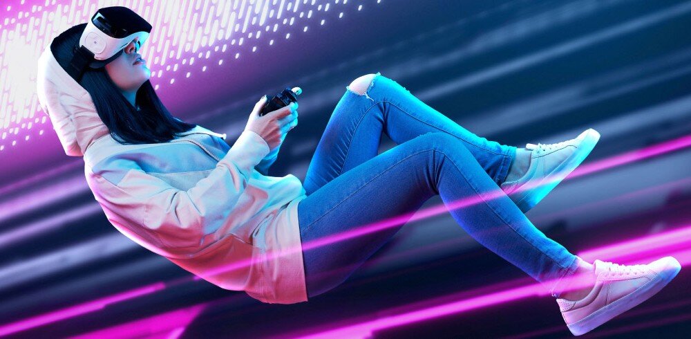 Płyta główna GIGABYTE Z890 Gaming X WiFi7 Osoba w jasnej bluzie z kapturem i goglach VR unosząca się w pozycji półleżącej z kontrolerem w dłoniach na tle różowo-fioletowych smug światła, łączność, LAN, Wi-Fi