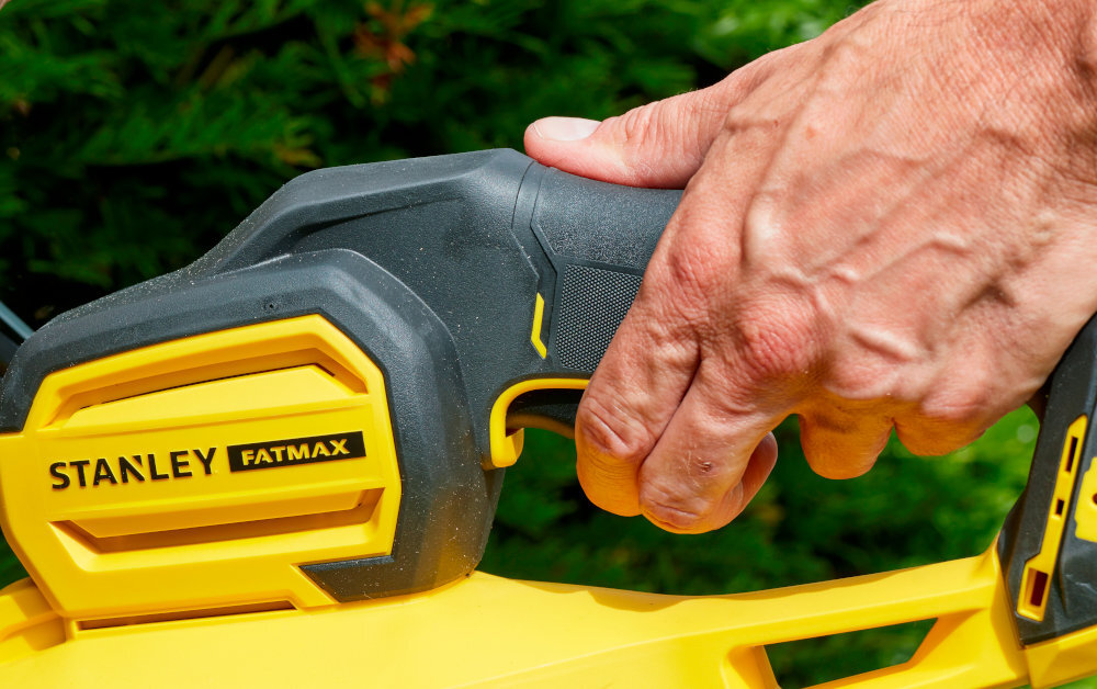 Nożyce do żywopłotu STANLEY SFMCHT855B-XJ 550mm 18V akumulatorowe żywopłot ogród zbliżenie na rękojeść główną osoba trzyma dłoń na rękojeści główny i pomocniczy uchwyt antypoślizgowa miękka powłoka rękojeści użytkownik może pewniej prowadzić nożyce ograniczając zmęczenie dłoni i nadgarstków