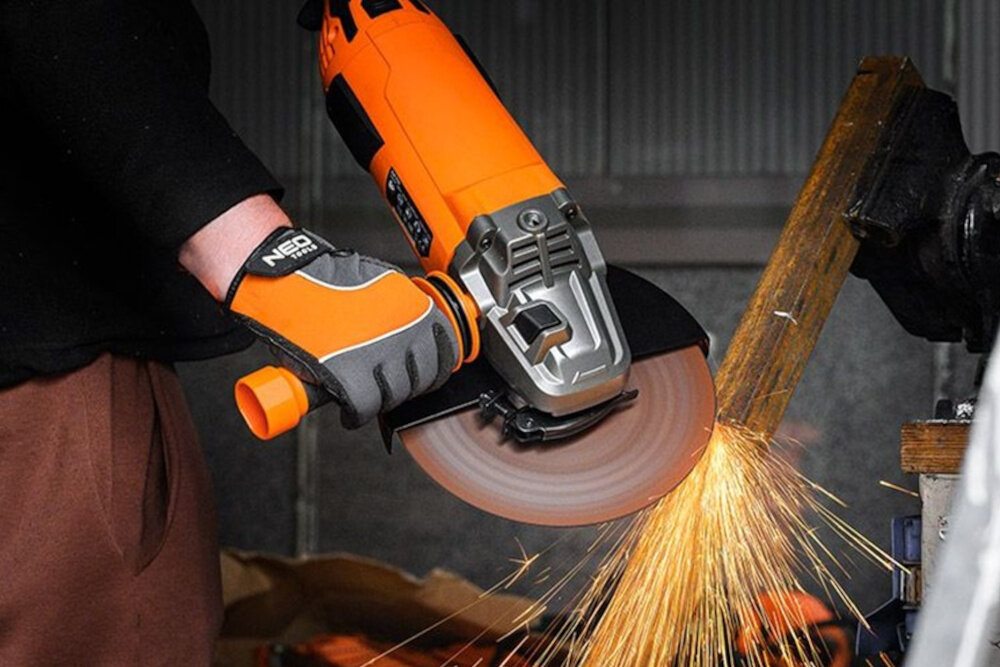 Szlifierka kątowa NEO 04-715 osoba trzyma szlifierkę w dłoniach szlifuje metalowy element iskry spod tarczy współpracuje z tarczami o średnicy 230 mm praca na większej powierzchni bez częstego przesuwania narzędzia efektywność i skraca czas operacji prędkość do 6600 obr./min płynne cięcie skuteczne szlifowanie