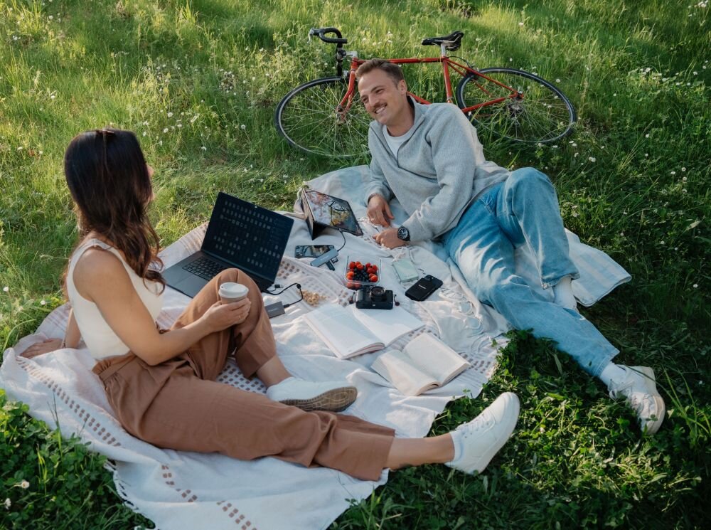 Dysk VERBATIM Metal Mini Kobieta i mężczyzna leżący na kocu w parku z laptopem, aparatem, telefonami i przekąskami, obok stoi rower, wymiary, metalowa obudowa, otwór na smycz