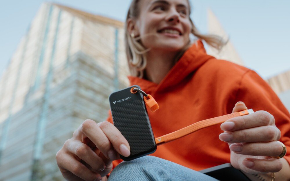 Dysk VERBATIM Pocket 2TB SSD Czarno-pomarańczowy kobieta stojąca przed budynkiem trzymająca dysk z rozwiniętym kablem z jednym końcem podłączonym do dysku opis