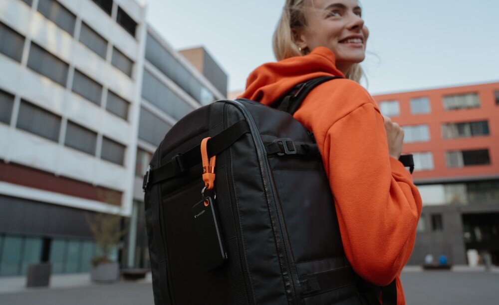 Dysk VERBATIM Pocket 2TB SSD osoba z odwrócona plecami z plecakiem, do którego przymocowany jest dysk Czarno-pomarańczowy brelok mocowanie uchwyt na kabel