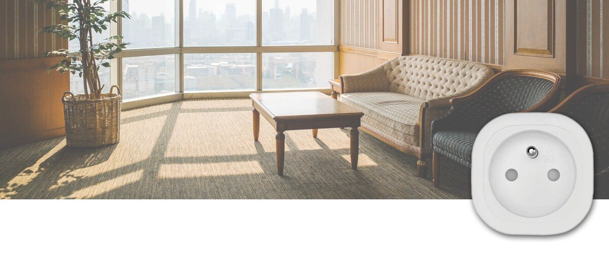 Inteligentne gniazdko OMAJIN Smart Plug SK, głos, komenda, aplikacje, geolokalizacja, w tle pokój gościnny, na pierwym planie w prawym dolnym rogu wtyczka frontem na wprost