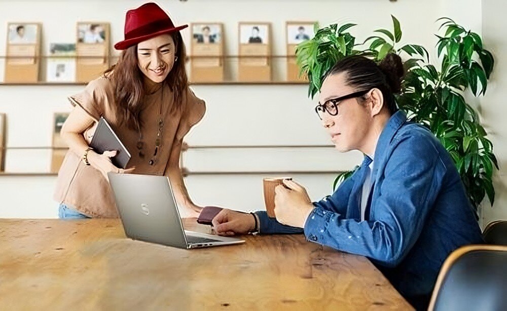 Laptop DELL Latitude 7340 Kobieta i mężczyzna rozmawiają przy stole w jasnym wnętrzu; mężczyzna korzysta z laptopa, kobieta trzyma tablet, przekątna, obudowa, materiał, wielkość