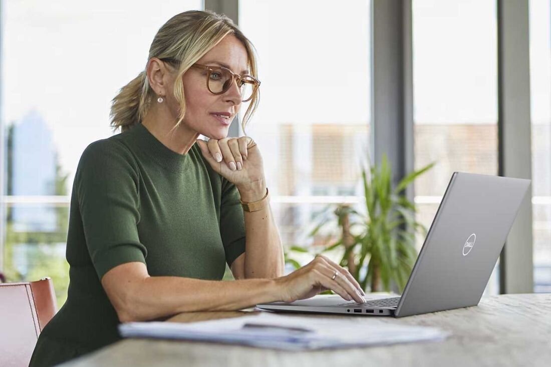 Kobieta w okularach siedzi przy stole z laptopem. - zaawansowana łączność Wi-Fi 7 Bluetooth 5.4