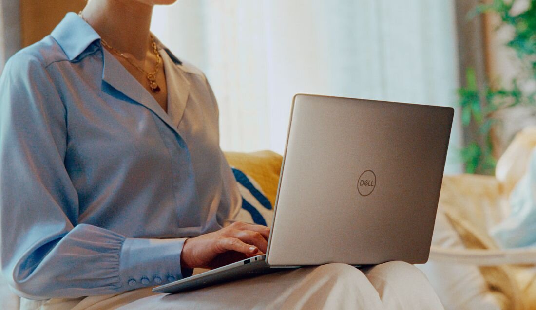 Kobieta w niebieskiej koszuli pracująca na laptopie Dell Latitude siedząc na sofie w jasnym, eleganckim salonie z poduszkami i dekoracyjnymi roślinami. - Cztery głośniki stereo