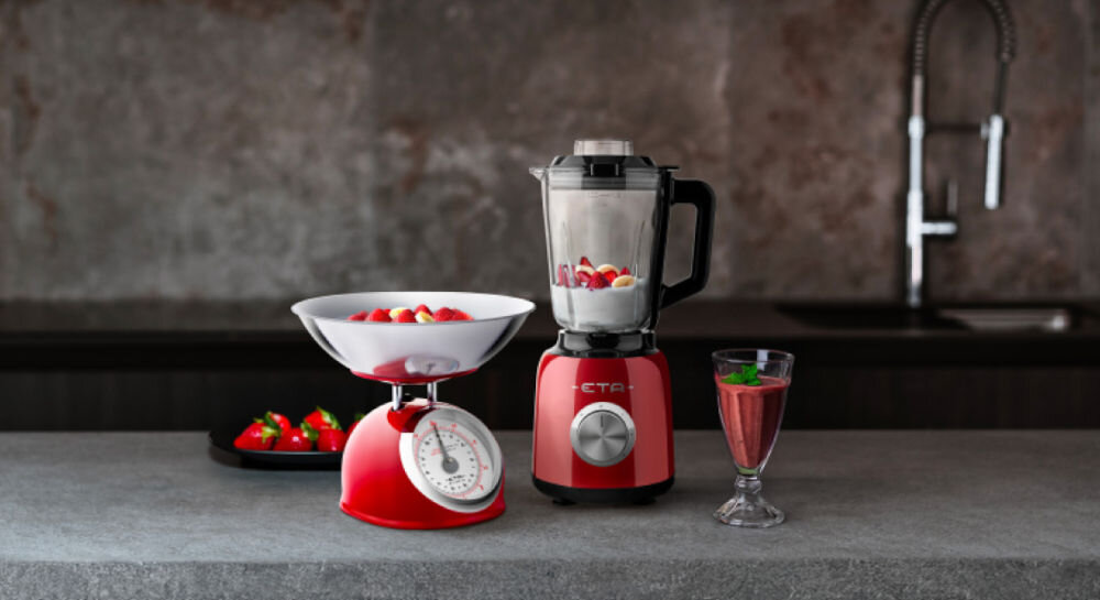 Blender kielichowy ETA Storio 901190020 Czerwony ciemne tło blender w kolorze czerwonym stoi na ciemnym blacie srebrne pokrętło w kielichu zawartość obok w kieliszku koktajl obok blendera stoi czerwona waga stylowy design wysoka funkcjonalność eleganckie stalowe wykończenie solidny szklany kielich o pojemności 1,5 litra koktajle kremowe zupy sosy kruszenie lodu otwór w pokrywie dolewanie płynów podczas pracy precyzyjna kontrola 