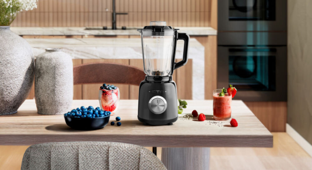 Blender kielichowy ETA Storio 901190030 Czarny do koktajli czarny blender stoi na blacie srebrne pokrętło czarna rączka kielich obok owoce w misce i napój w szklance 