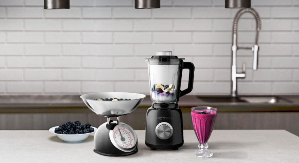 Blender kielichowy ETA Storio 901190030 Czarny ciemne tło blender w kolorze czarnym stoi na blacie srebrne pokrętło w kielichu zawartość obok w kieliszku koktajl obok blendera stoi czarna waga stylowy design wysoka funkcjonalność eleganckie stalowe wykończenie solidny szklany kielich o pojemności 1,5 litra koktajle kremowe zupy sosy kruszenie lodu otwór w pokrywie dolewanie płynów podczas pracy precyzyjna kontrola 