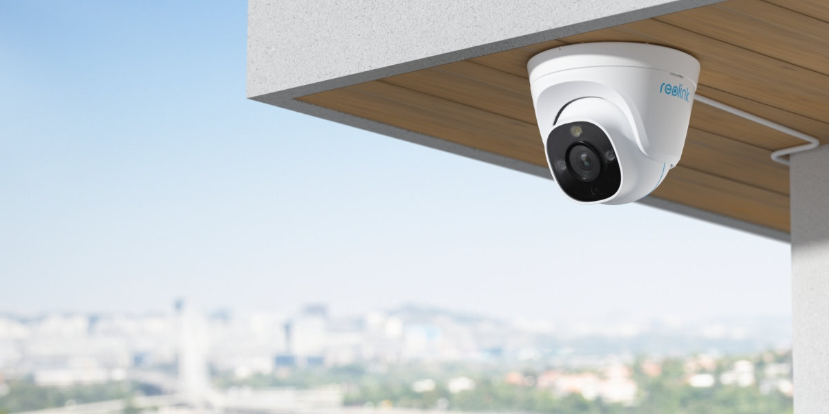 Kamera REOLINK P334 kamera zawieszona pod dachem na rogu domu z widokiem na miasto
